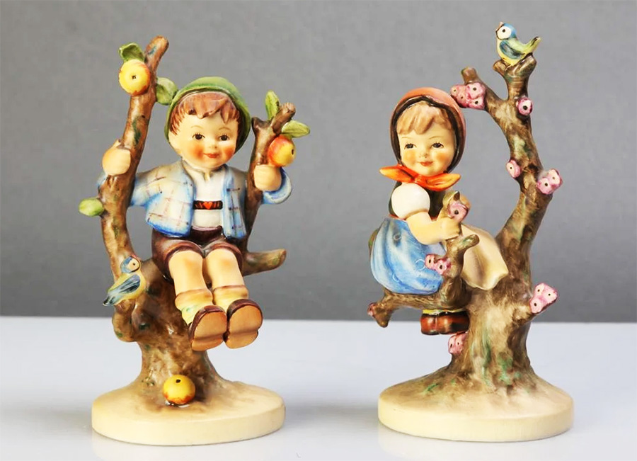 Vintage collectible Hummel figurines depicting a boy and a girl sitting in apple trees.